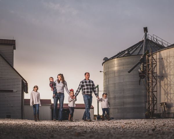A family is walking in front of a grain silo holding hands.