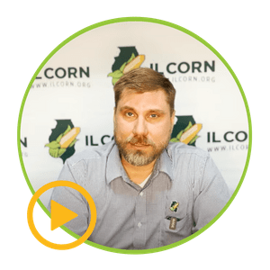A man is sitting in front of a sign that says corn