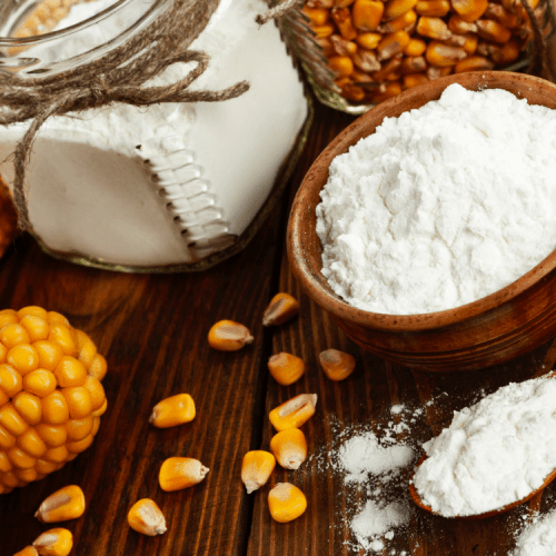A wooden table with bowls of corn flour and corn on the cob