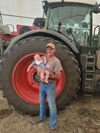 A man is holding a baby in front of a tractor