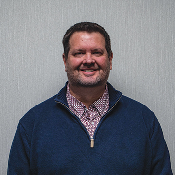 A man in a blue sweater and polka dot shirt is smiling for the camera.