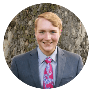 A man in a suit and tie is smiling in front of a tree