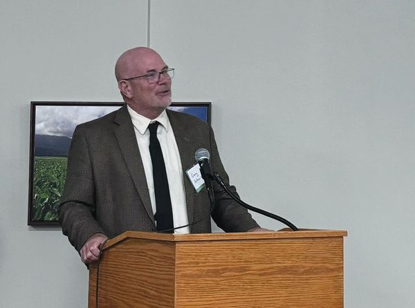 A man in a suit and tie is standing at a podium speaking into a microphone.