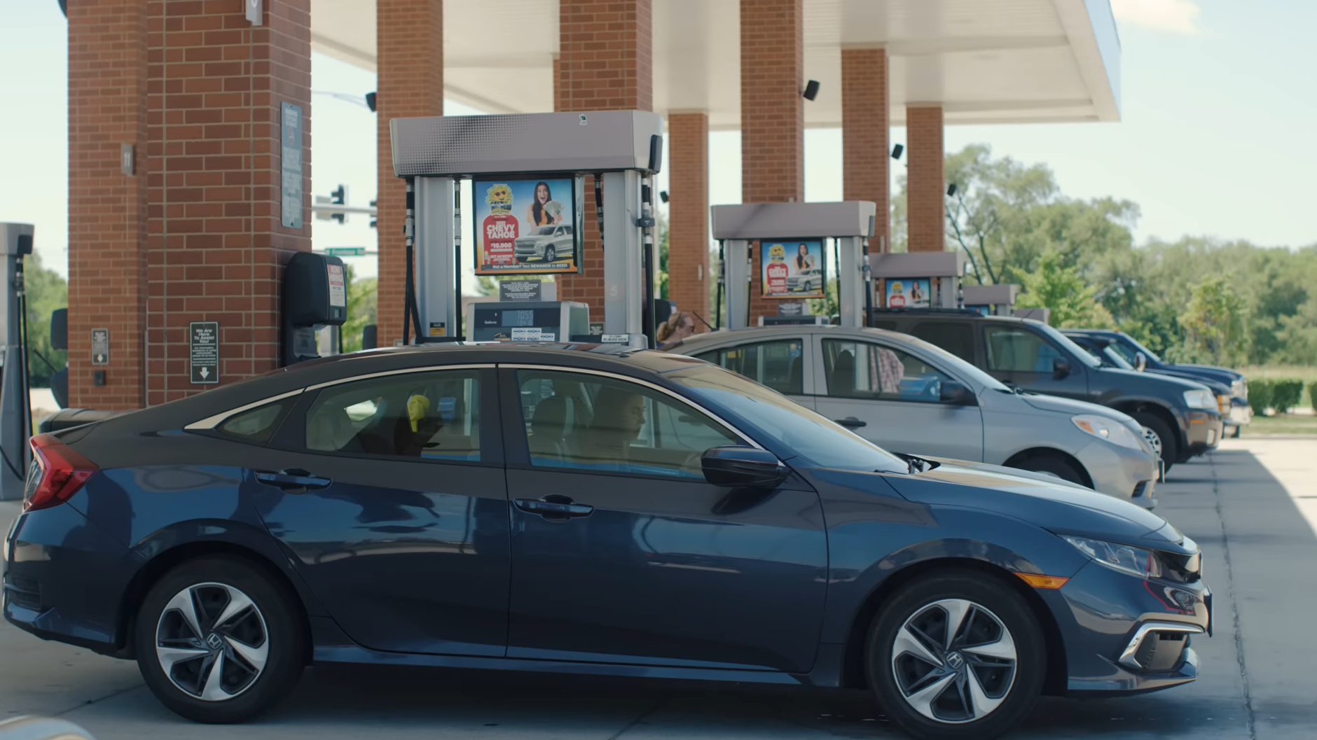 A row of cars are parked at a gas station.