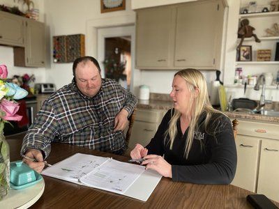 A man and a woman are sitting at a table in a kitchen looking at a book.