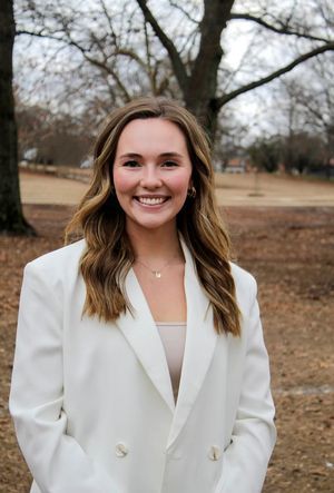 The woman is wearing a white jacket and smiling for the camera.