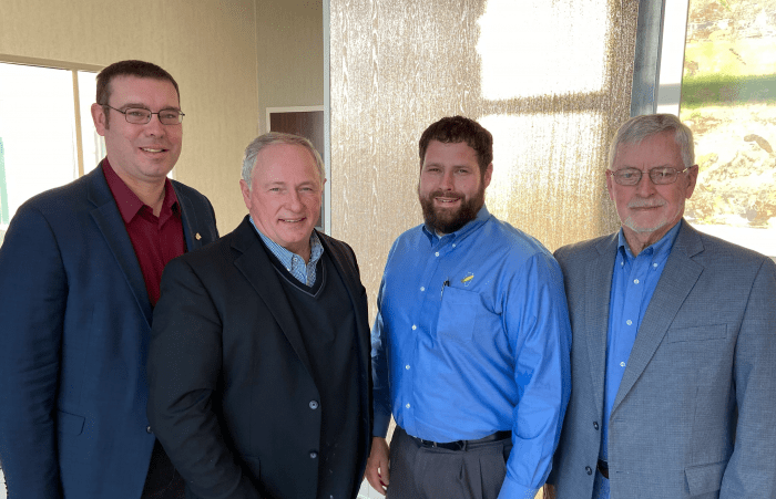 Four men in suits and shirts are standing next to each other in a room.