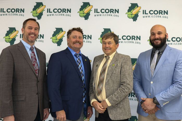 Four men are standing in front of a wall that says ilcorn