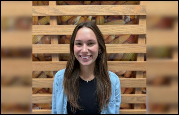 A woman in a blue sweater is smiling in front of a wooden wall.
