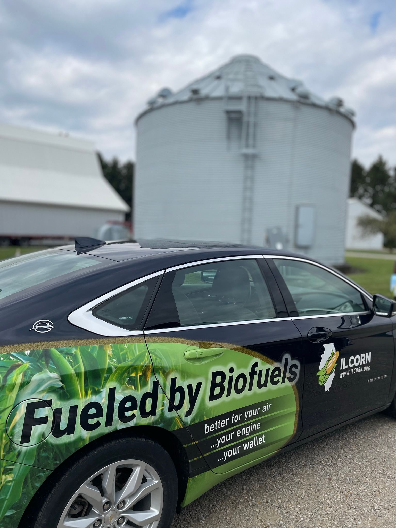 A car that is fueled by biofuels is parked in front of a silo.