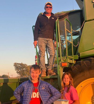 A man and two children are standing on top of a green tractor.