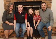 A family is posing for a picture in front of a fireplace.