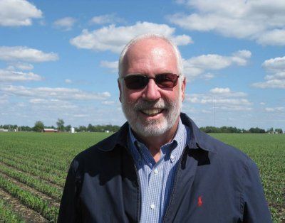 A man wearing sunglasses and a polo shirt is standing in a field.