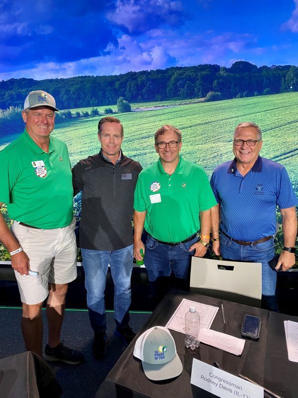 A group of men in green shirts are standing around a table.
