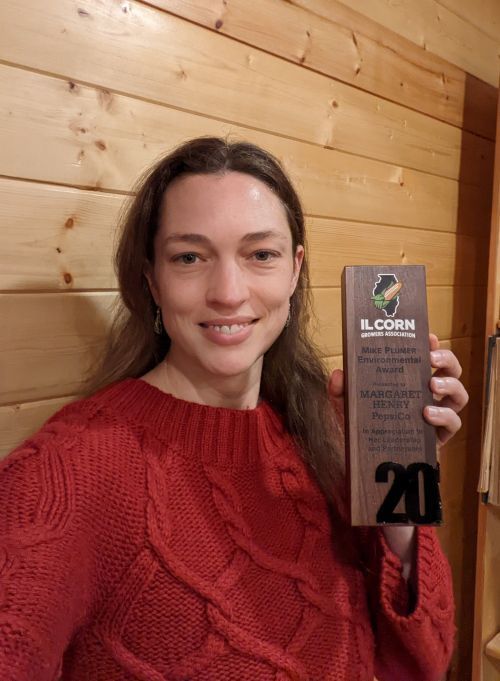A woman in a red sweater is holding a wooden plaque with the number 20 on it.