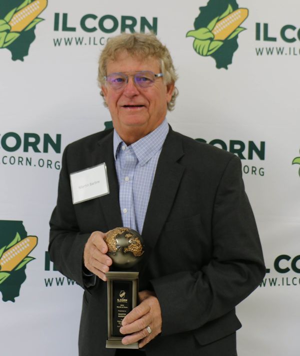 A man in a suit is holding a trophy in front of a banner that says ilcorn