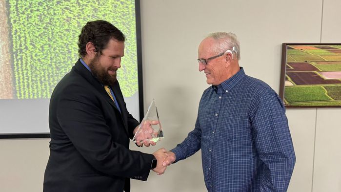 Two men are shaking hands and one is holding an award.