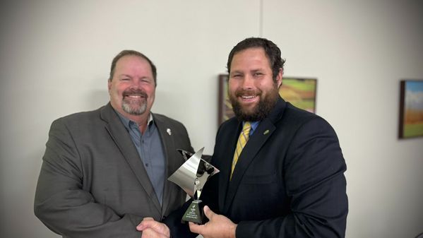 Two men in suits are shaking hands while holding a trophy.