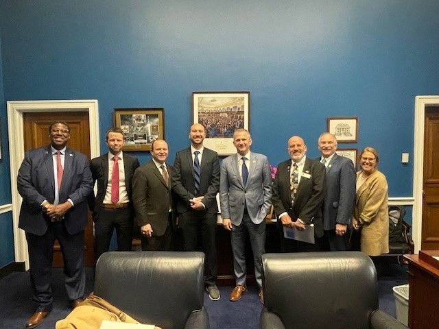 Group of people in suits posing in a room with blue walls, two leather chairs in the foreground.