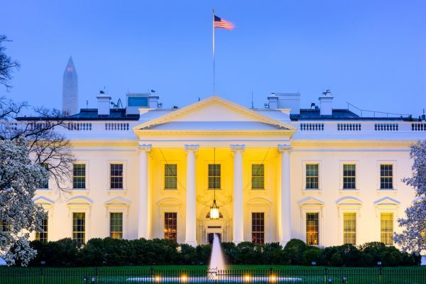 The white house is lit up at night and has a flag on top of it.