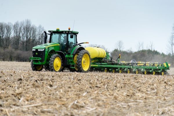 A green and yellow john deere tractor is plowing a field.