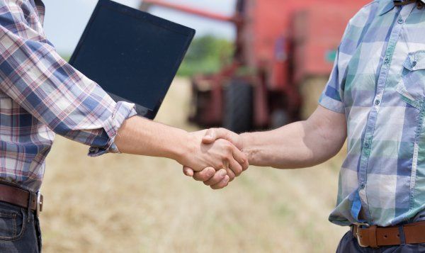 Two men are shaking hands in a field with a tractor in the background.