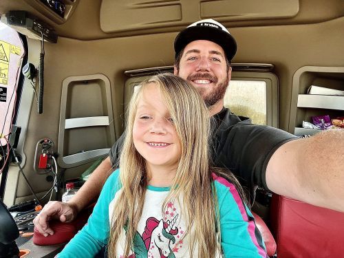 A man and a little girl are taking a selfie in a truck.