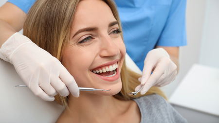 A woman is smiling while having her teeth examined by a dentist.