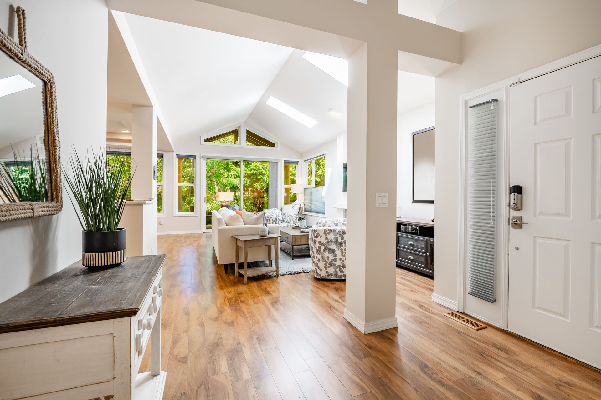 Bright open living room with vaulted ceiling, white walls, wood floors, and large windows overlooking greenery