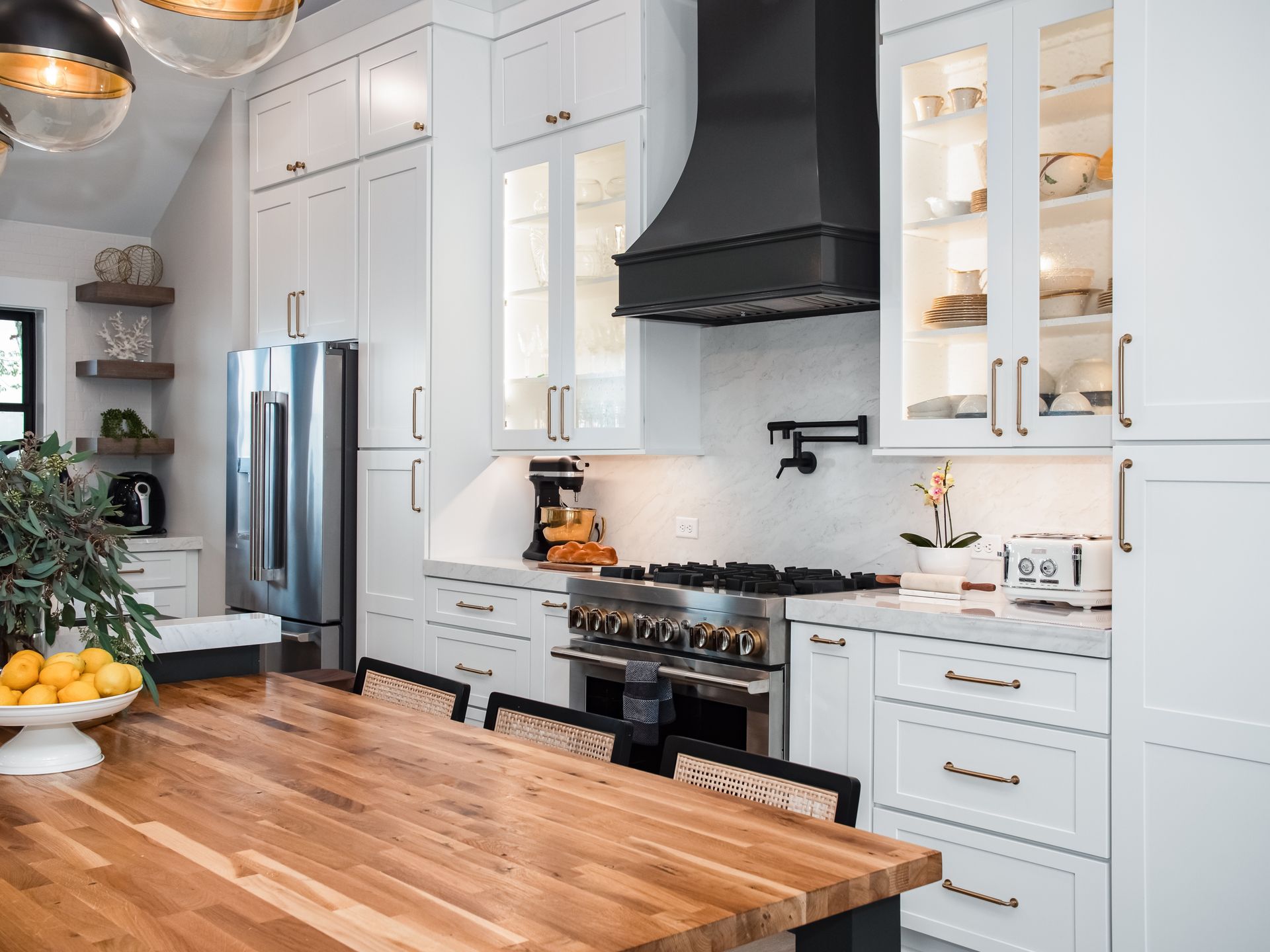 Bright modern kitchen with white cabinets, black range hood, stainless fridge, and wooden island countertop