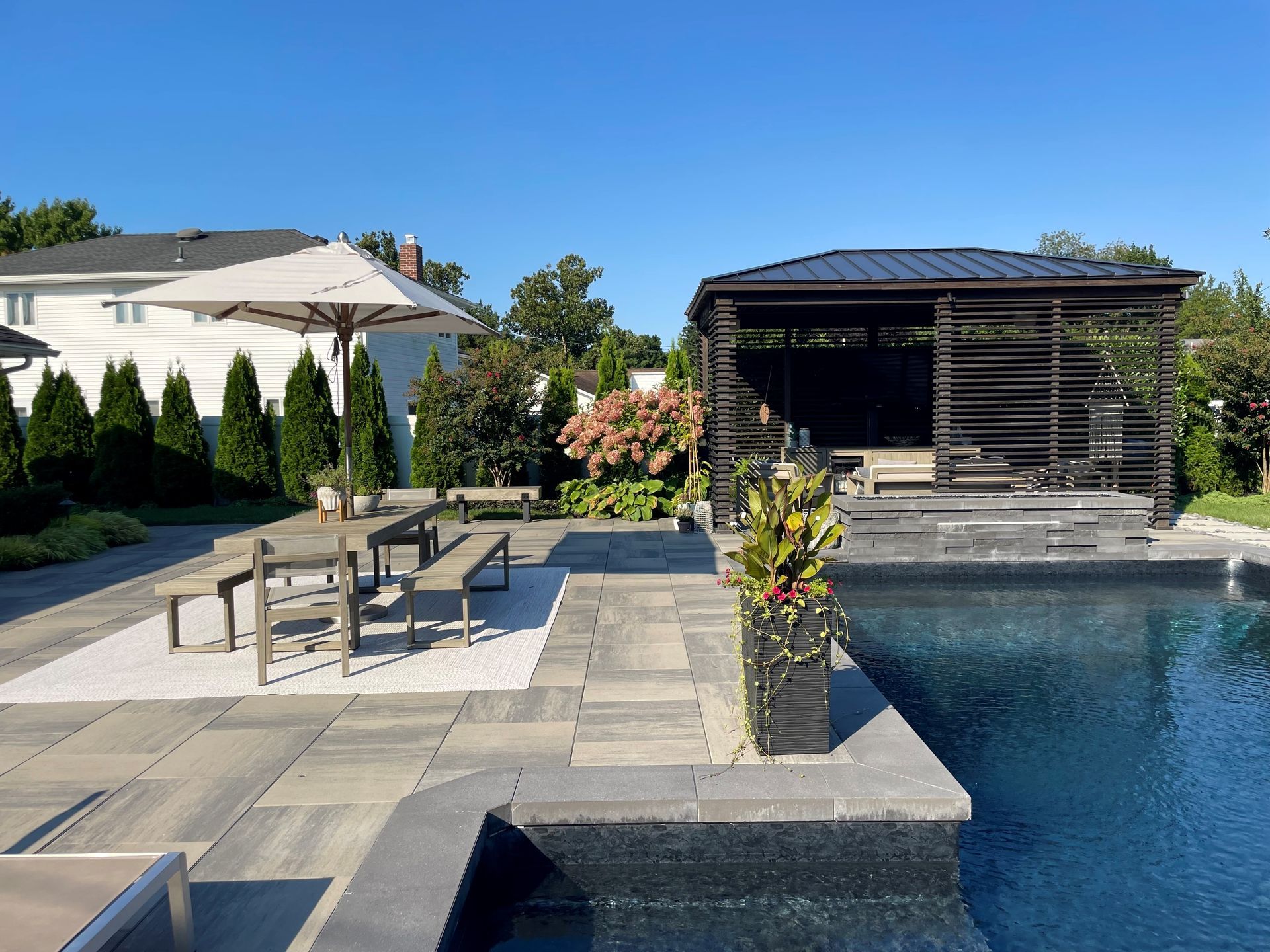 Modern backyard patio with pool, lounge chairs, dining table, and a shaded gazebo