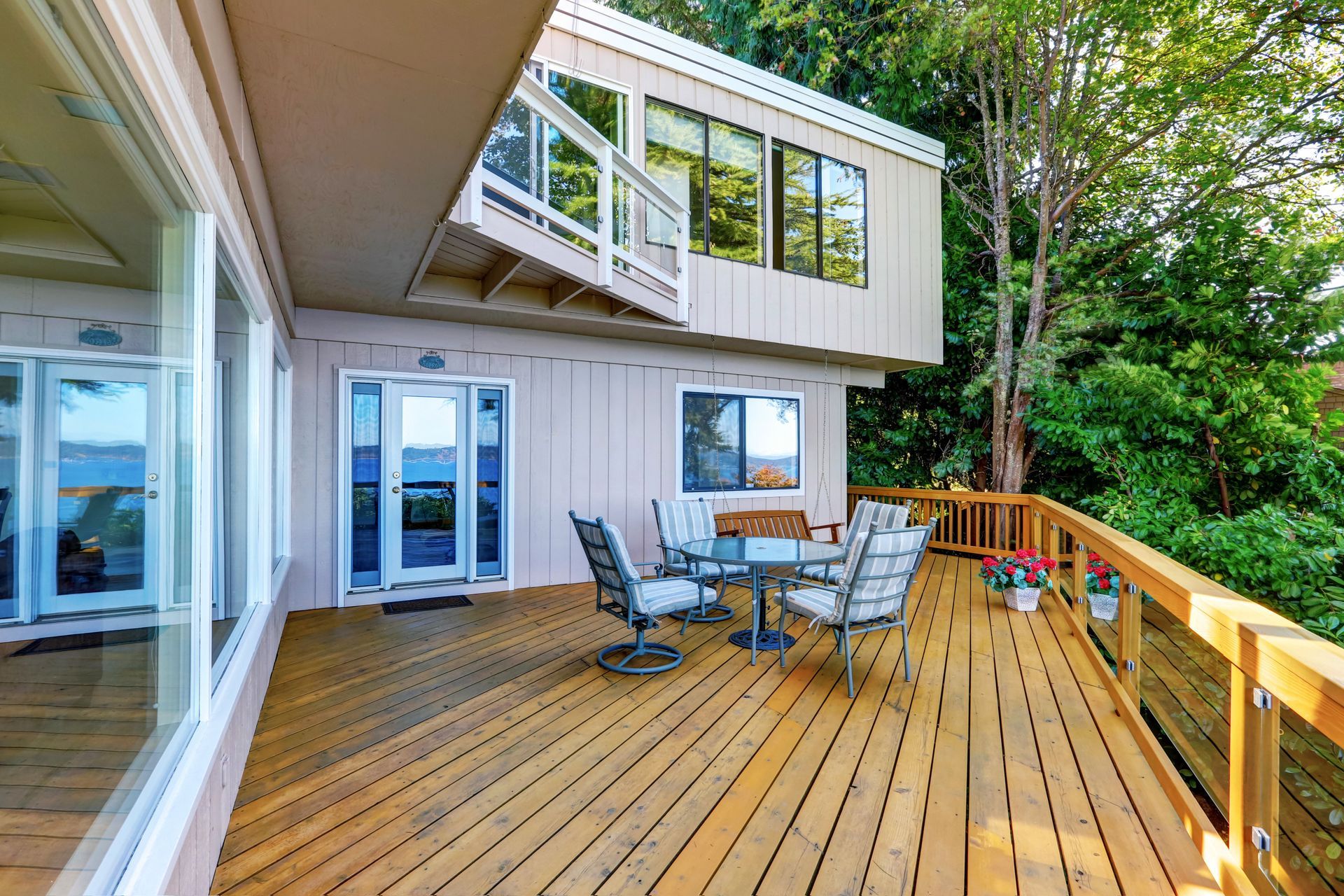 Wooden deck with patio table and chairs beside a house, overlooking trees and water