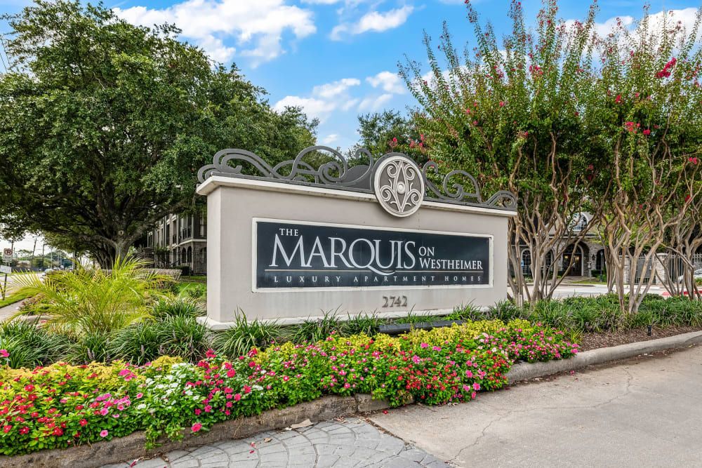 a sign surrounded by flowers and trees at Marquis on Westheimer in Houston, TX.