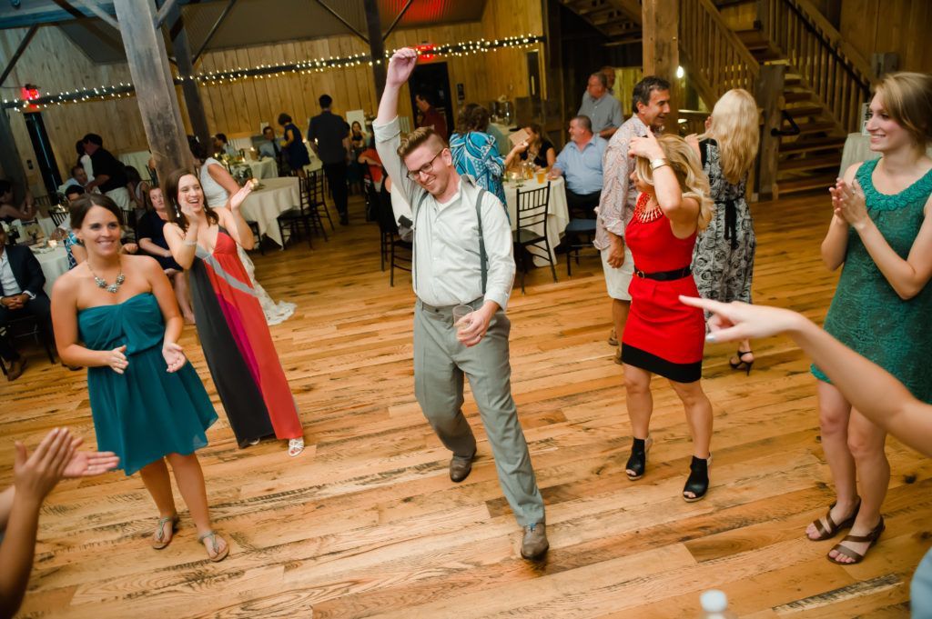 Bride being lifted up at a wedding reception, arms raised, smiling. Guests cheer in an ornate room.