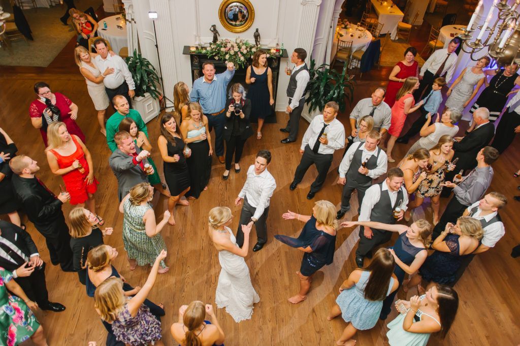 Wedding reception with bride and groom dancing, surrounded by guests. People are celebrating, arms raised.