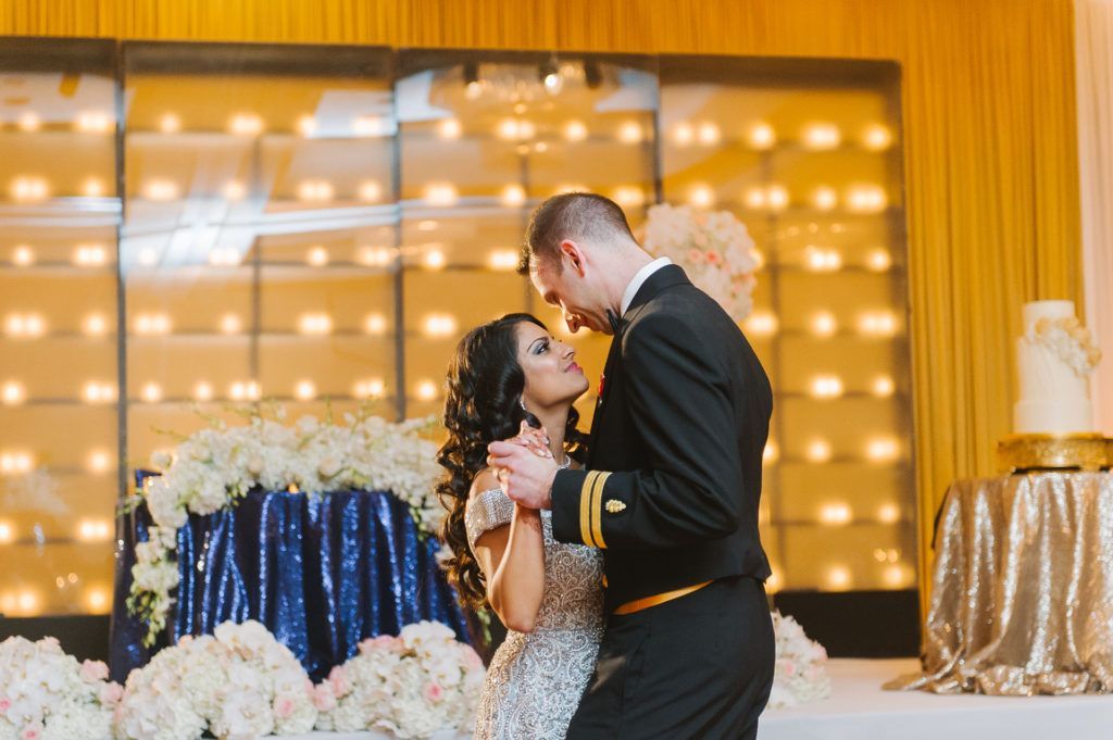 Bride and groom dancing at wedding reception with sequined tablecloths and wall of lights.