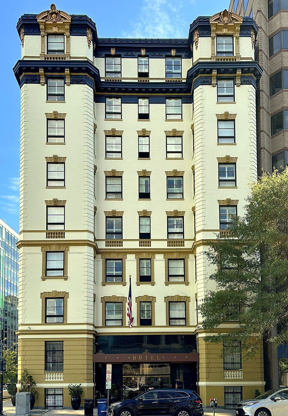 Ivory brick building with dark blue trim, ornate top. Cars parked out front.