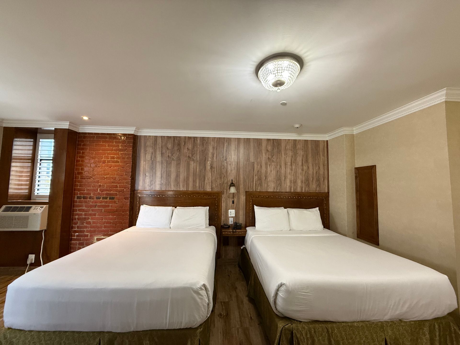 Two double beds in a hotel room with exposed brick, wood accent wall, and a decorative ceiling light.