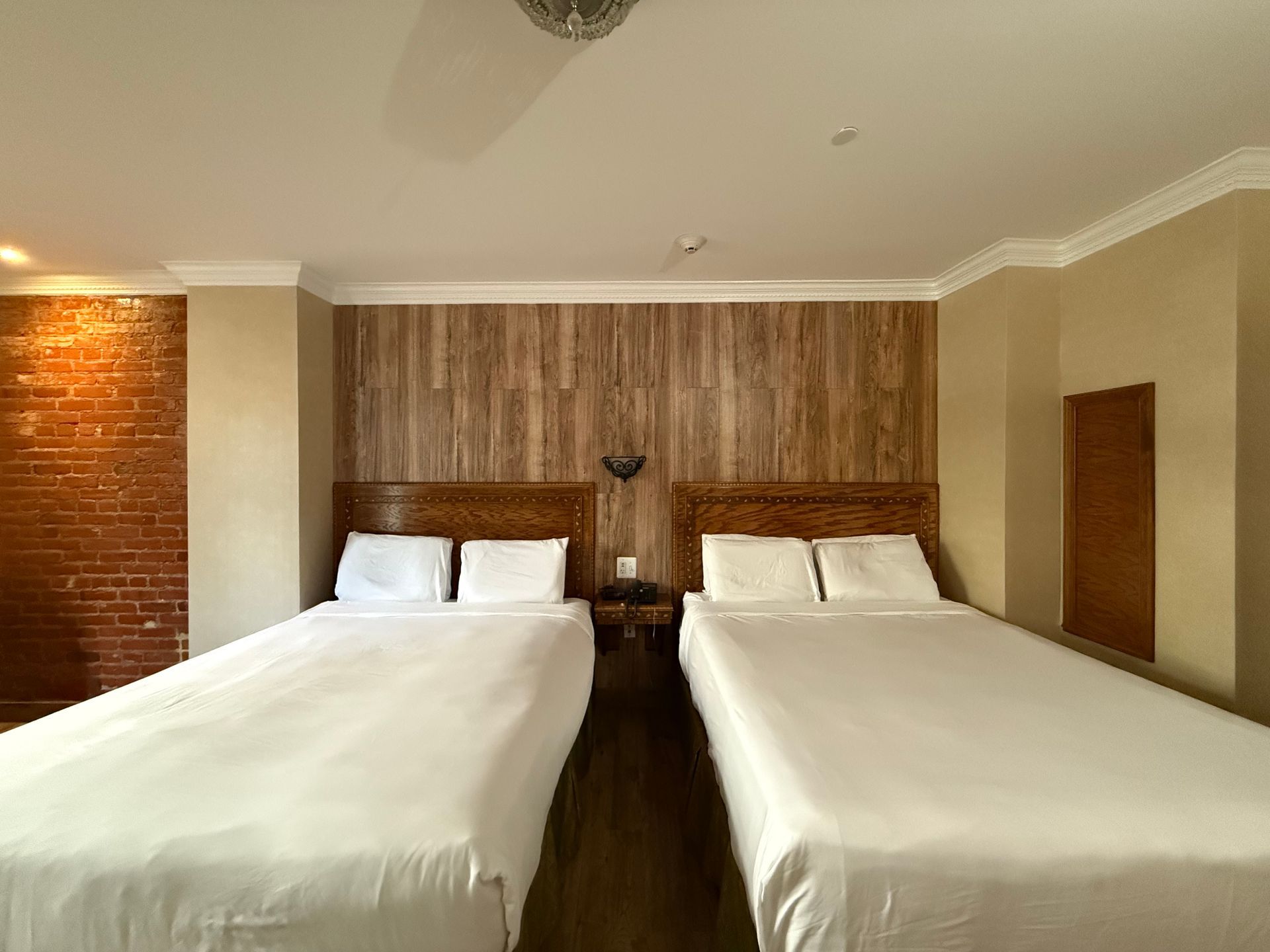 Two beds in a hotel room with wood and brick walls, a nightstand, and ceiling fan.