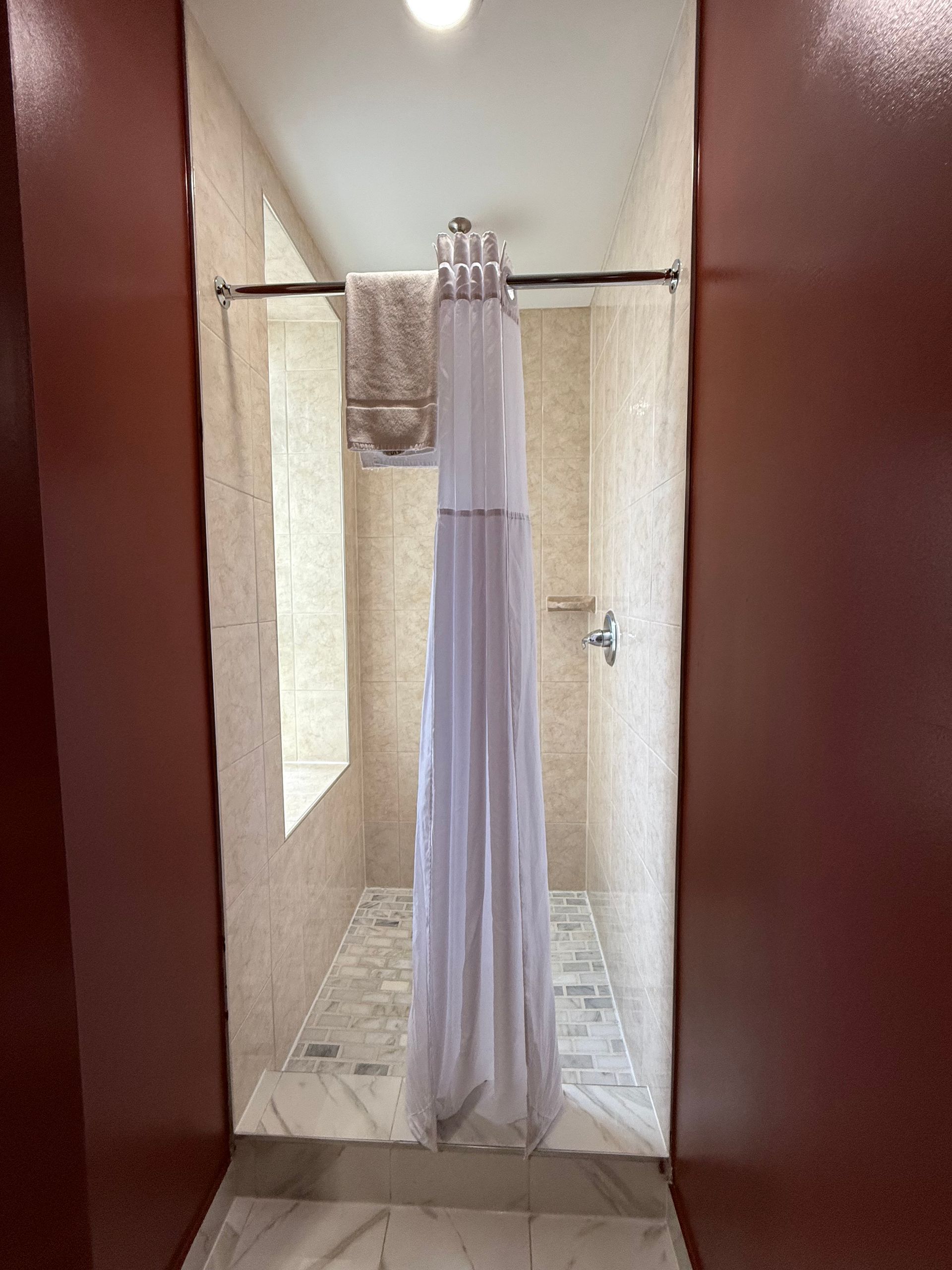 A walk-in shower with a light-colored curtain and a towel on a rod; tan walls are visible.