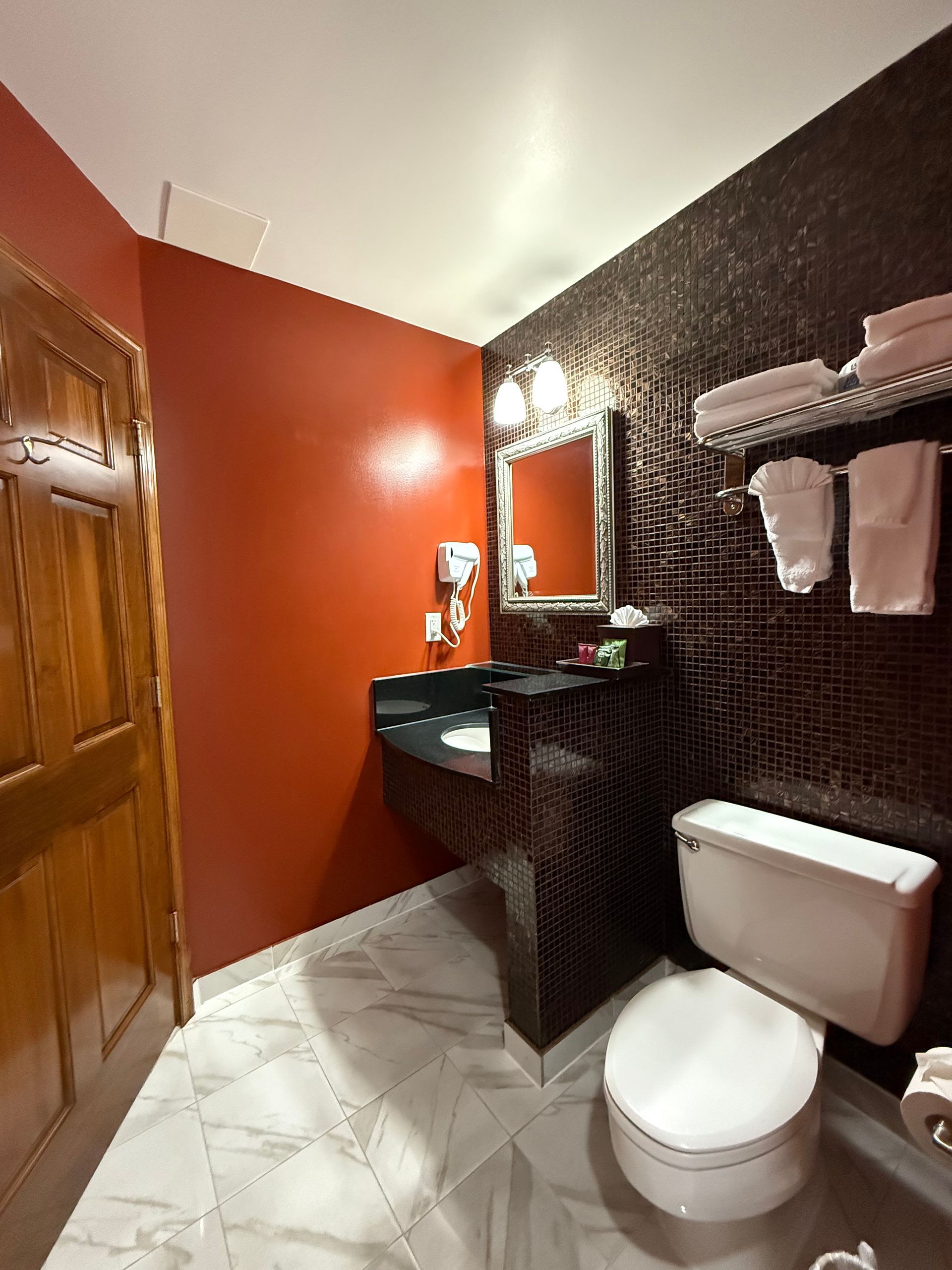 Bathroom with red and textured brown walls, toilet, sink, towels, mirror, and door.