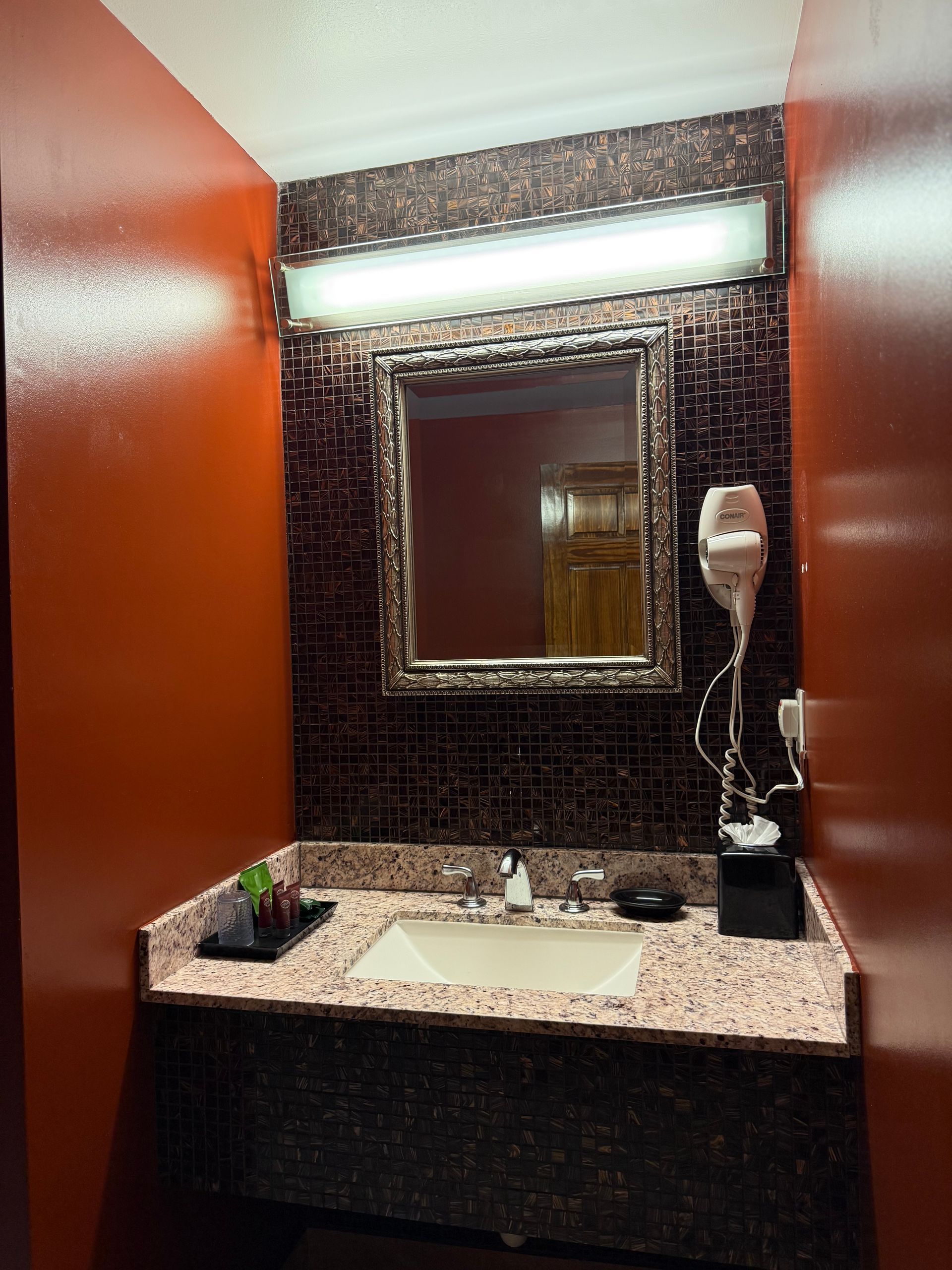 Bathroom with red walls, vanity with sink and mirror, brown textured backsplash, and a hair dryer.