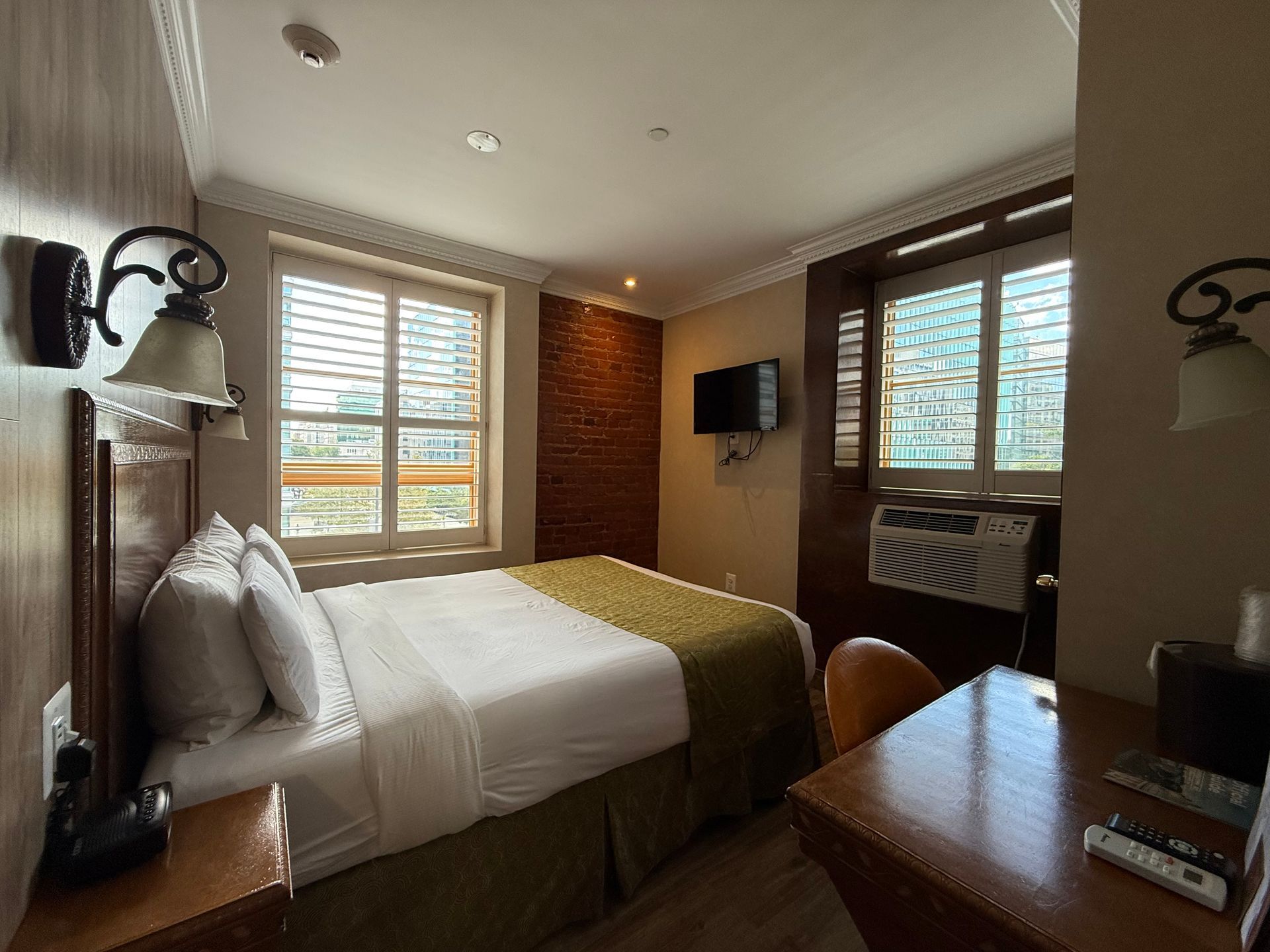 Hotel room with a bed, desk, and windows, with natural light.