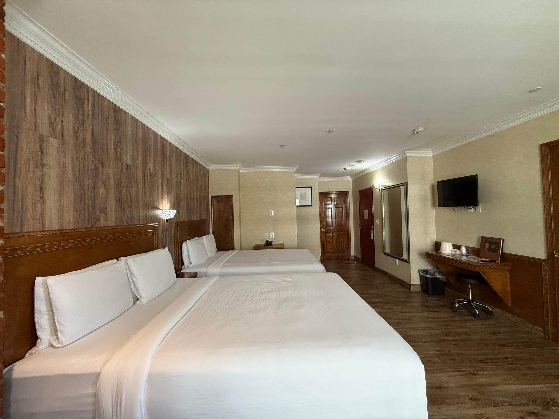 A hotel room with two large beds, wood paneling, a desk, and a TV.