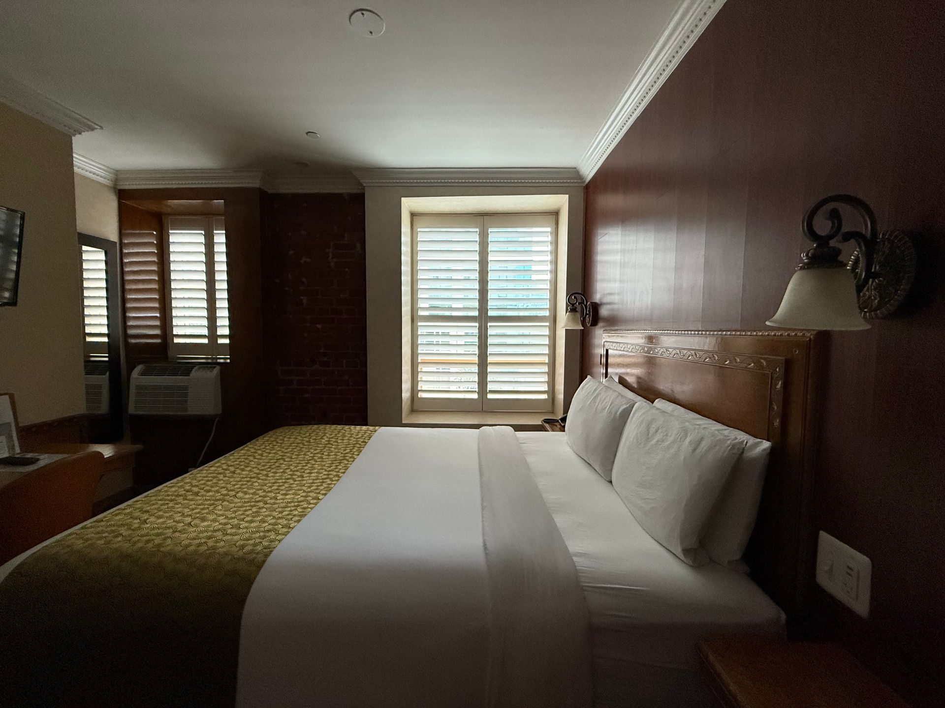 Hotel bedroom with king-size bed, window with shutters, and a dark red wall.