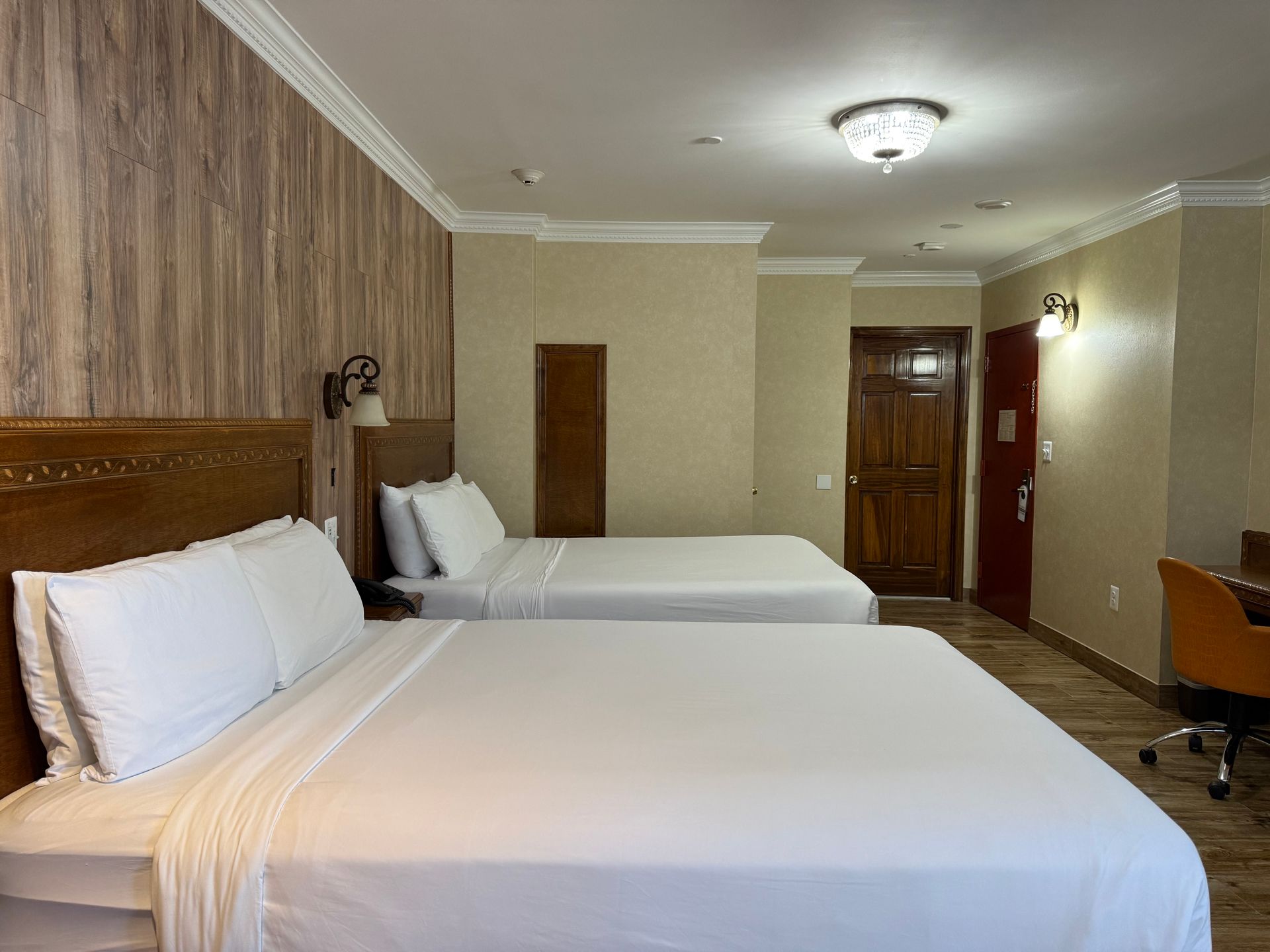 Hotel room with two queen beds, wooden headboards, and a desk.