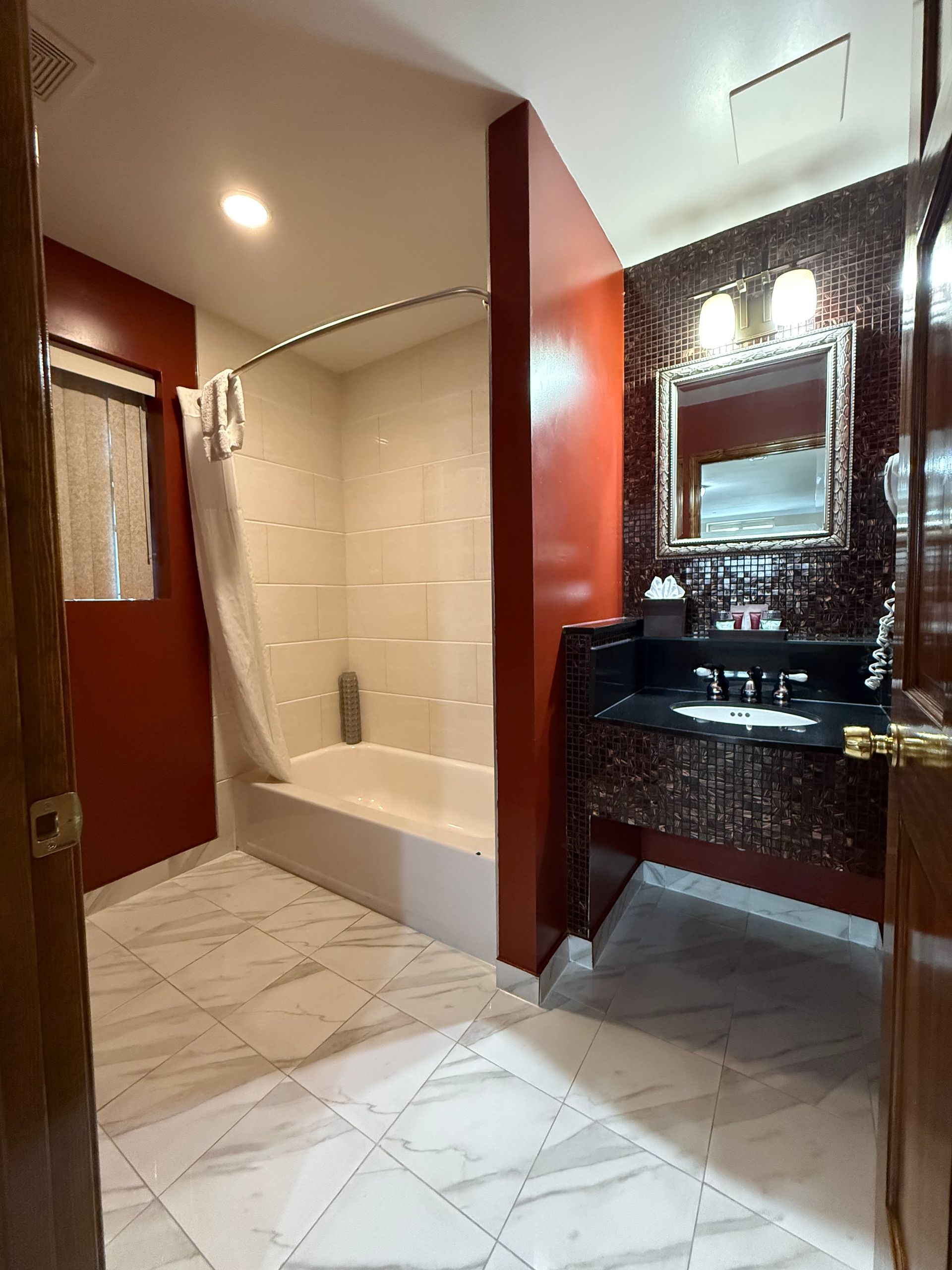 Bathroom with a red accent wall, white marble floor, shower, and vanity with a mirror.