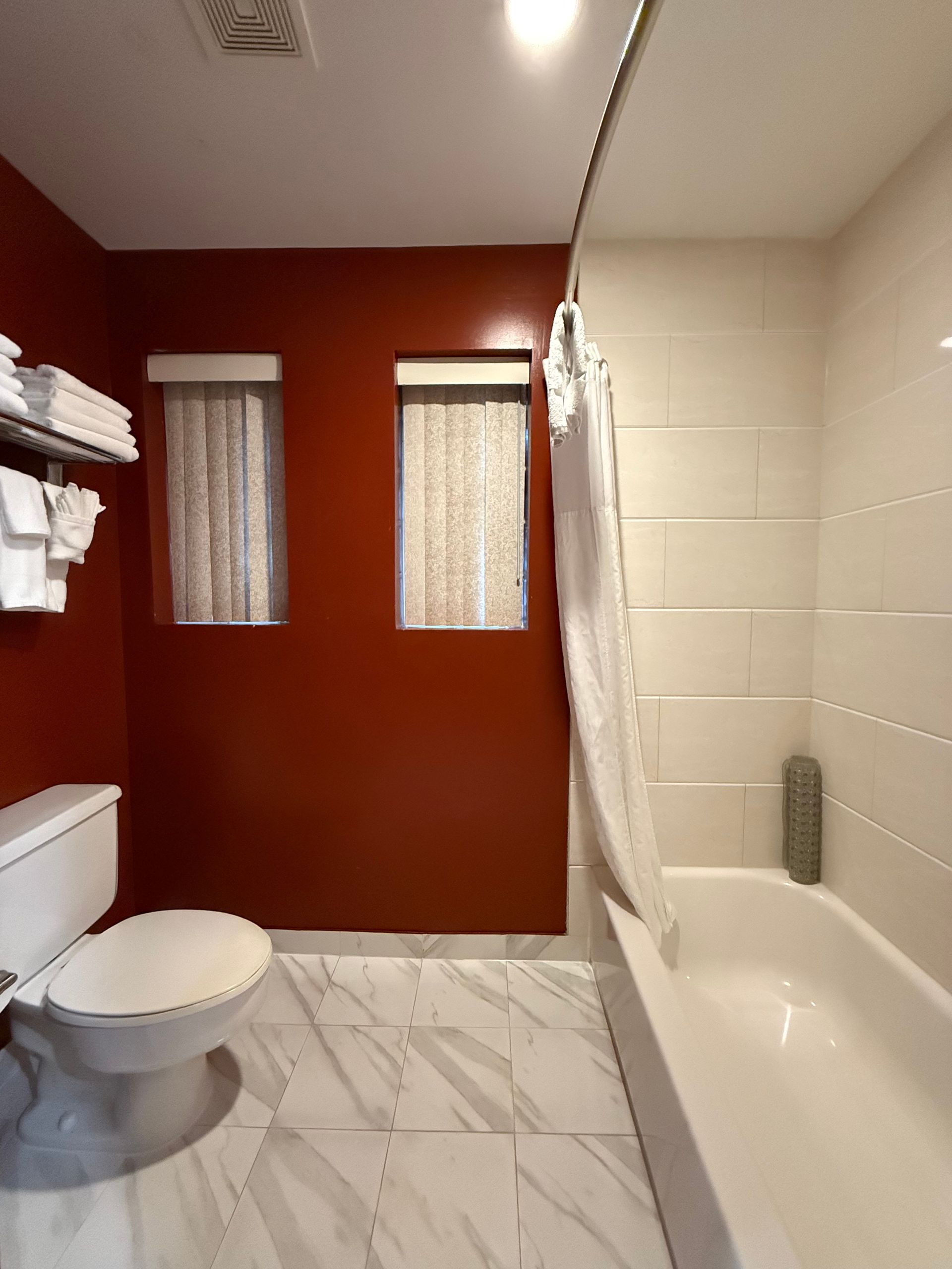 Bathroom with red walls, white tiled floor, toilet, and shower/tub with curtain.