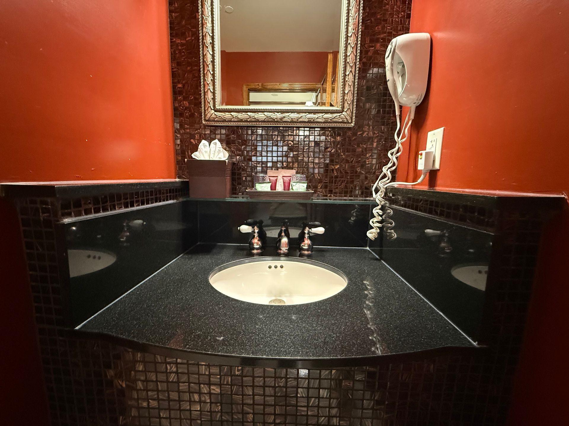 Bathroom sink with black countertop, red walls, and mosaic tile backsplash.