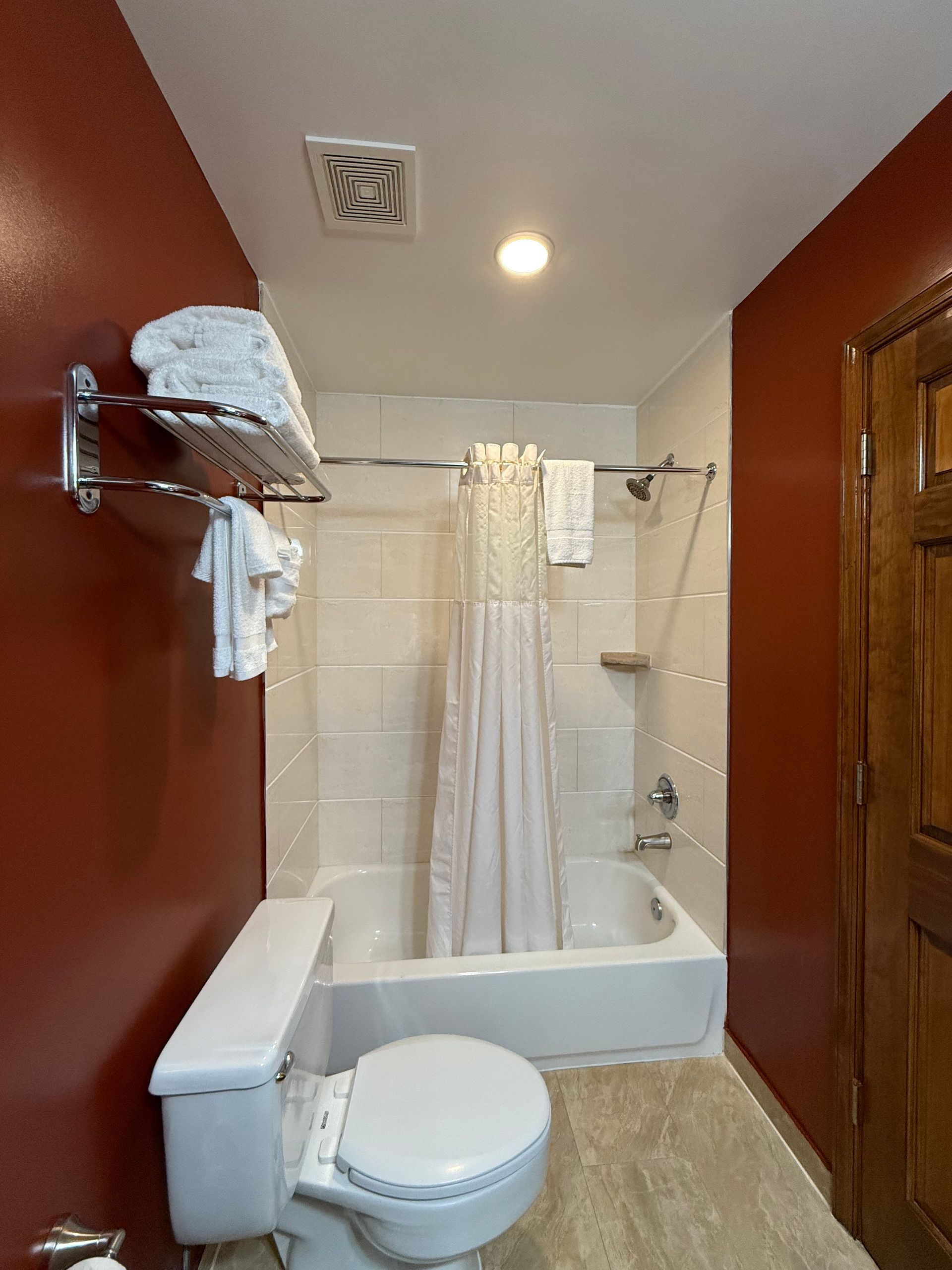 Bathroom with a white bathtub, toilet, and red walls. White towels are on a rack.